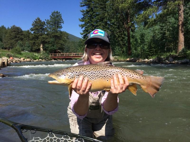 Female angler holding a large brown trout she caught while fly fishing on private water in Colorado with North Fork Ranch Guide Service.