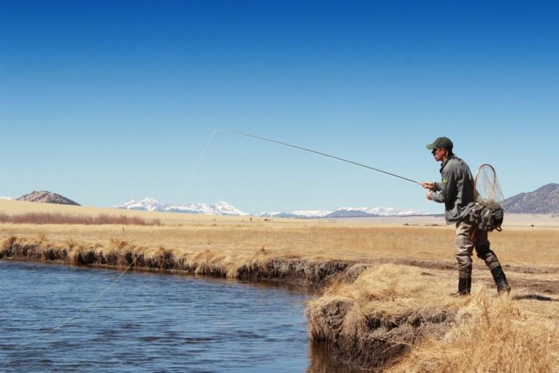 Angler casts a fly rod from the bank of a mountain river