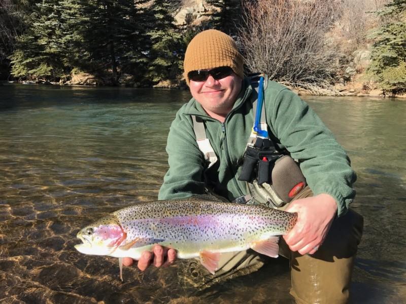 Smiling fisherman kneeling in the water and holding a huge rainbow trout