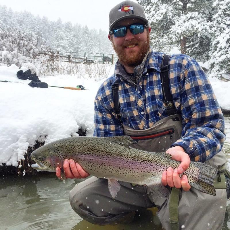 Man holding large trout just above the water while it's snowing