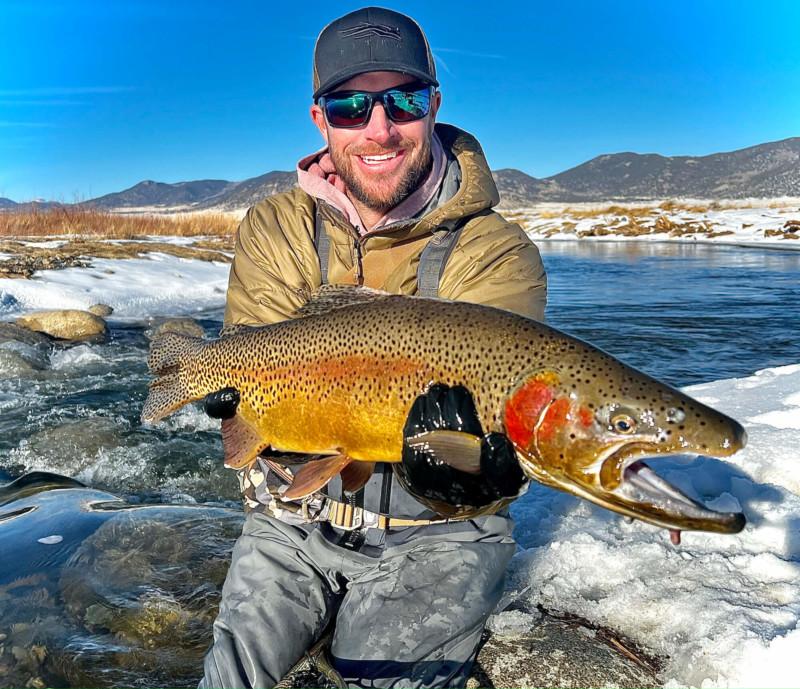 Angler displaying large brown trout caught in the frigid winter river